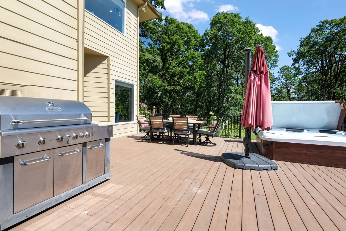 A backyard gathering space with a grill, hot tub, and outdoor dining table set against a natural backdrop. The area is ideal for barbecues, al fresco dining, or taking in the sights and sounds of the estate after a day of adventure.