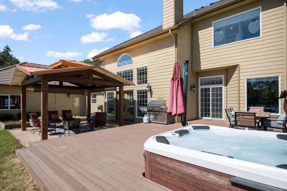 A close-up of the outdoor deck with a bubbling hot tub under a pergola, stylish seating, and a grill. Guests are depicted enjoying the space during sunset, creating a relaxed and social atmosphere ideal for group gatherings and celebrations.