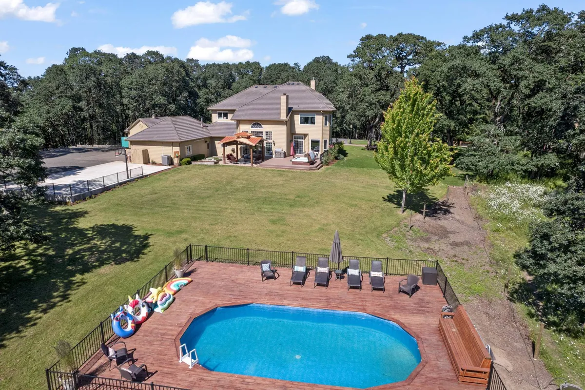 A sparkling in-ground pool surrounded by a deck with lounge chairs, set on an expansive lawn beside the house. The scene captures the relaxed mood of swimming, sunbathing, and outdoor gatherings.