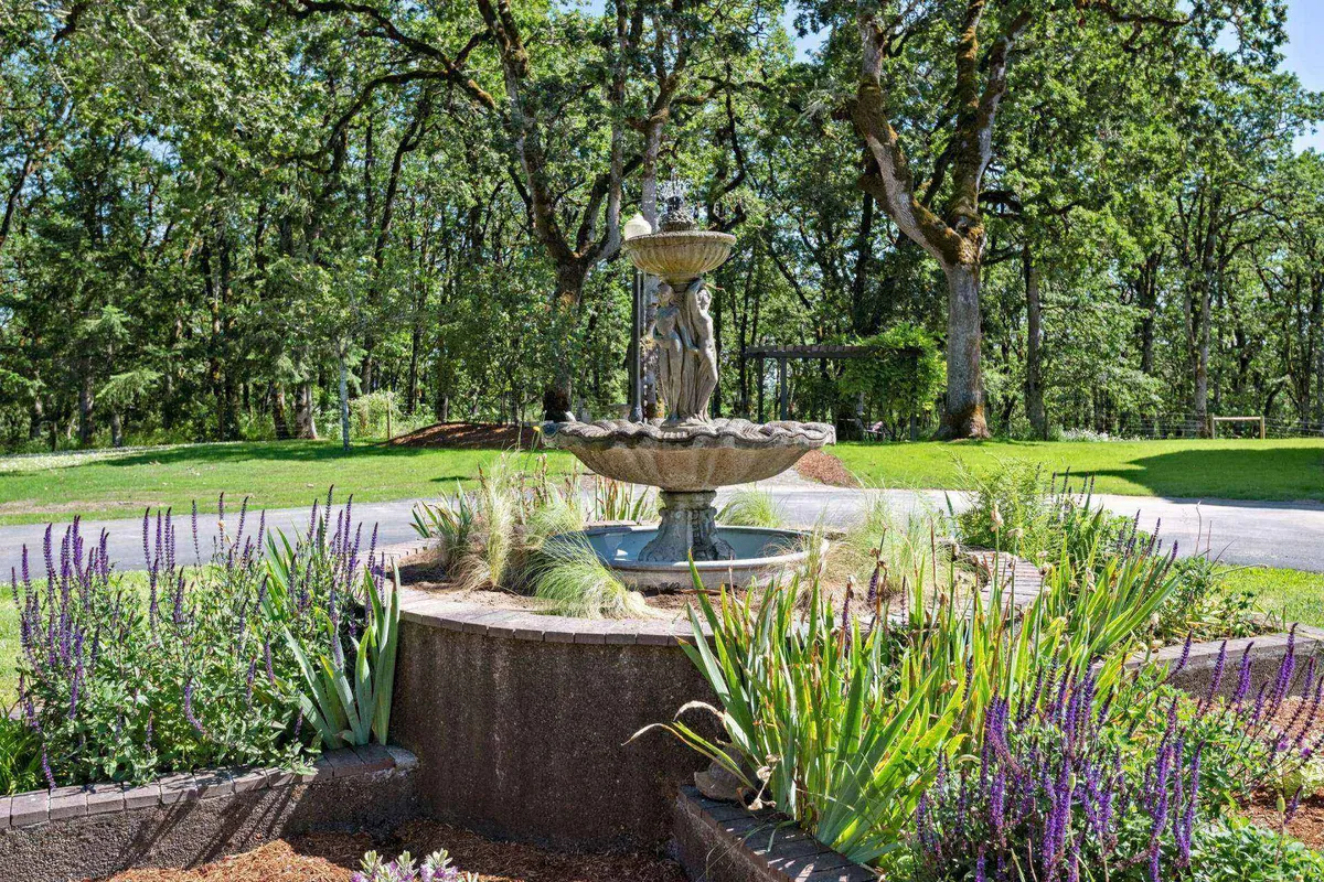 A calming garden scene with a prominent fountain, flourishing flower beds, and dense greenery, offering a picturesque spot for wildlife viewing or quiet reflection. The space is inviting and serene, perfect for meditative activities or peaceful escape.