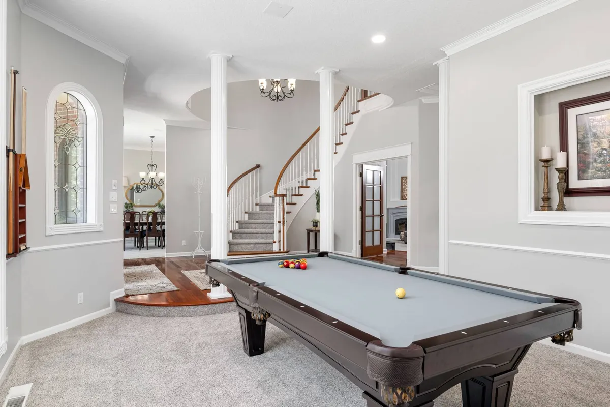 A stylish game area featuring a pool table, elegant chandelier, decorative artwork, and a staircase. The layout is ideal for socializing, playing billiards, and creating lively, memorable moments with family and friends.