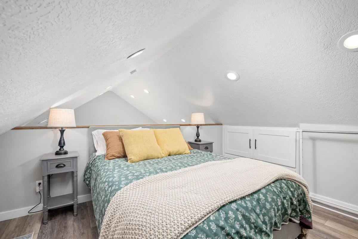 A serene bedroom with a plush bed adorned with decorative pillows and nightstands with lamps on either side. The overall atmosphere is inviting and tranquil, suggesting a restful night's sleep and a romantic, private retreat.