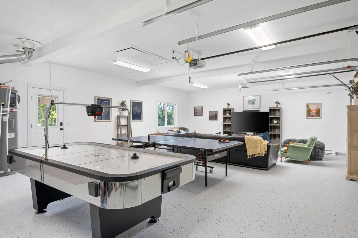 A vibrant game room featuring both an air hockey table and a ping pong table, with comfortable seating and engaging wall art. The setup invites guests to playful competition or relaxed spectating, all within a stylish, welcoming space.