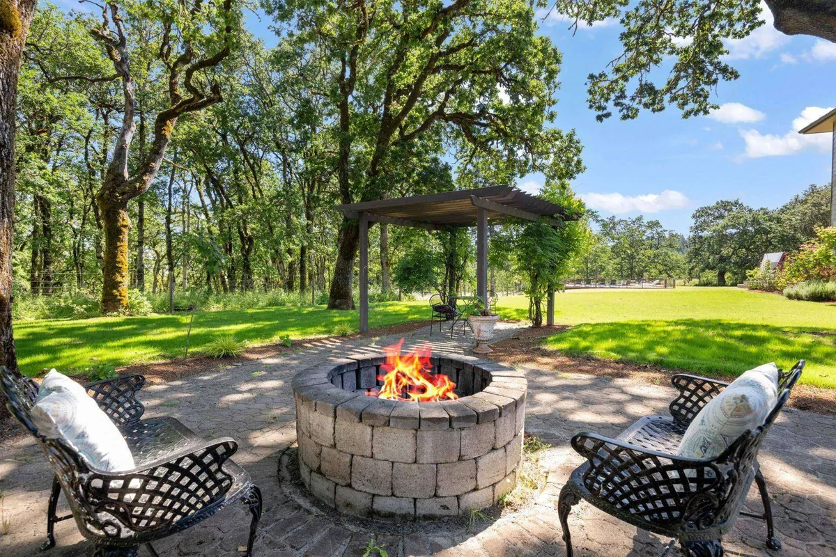 A cozy fire pit area with surrounding chairs beneath a canopy, nestled in lush greenery. The setting is intimate and inviting, ideal for storytelling, s'mores, or stargazing under the night sky.