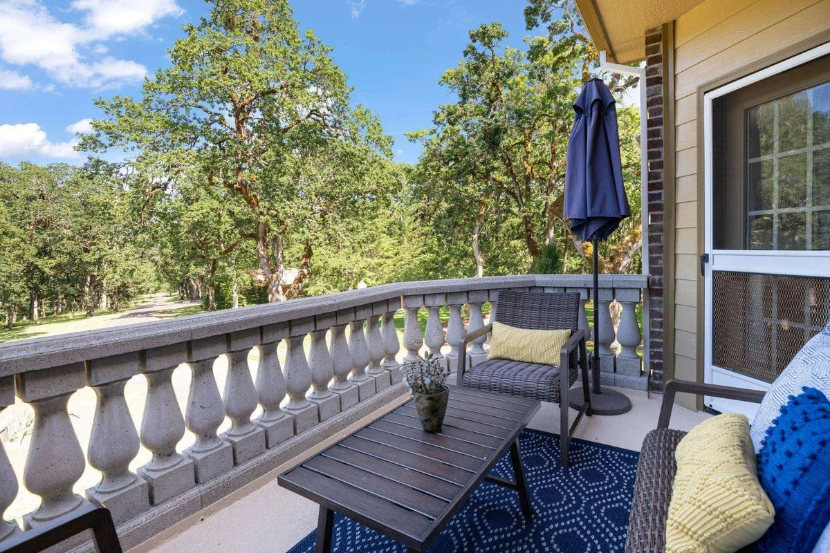 A peaceful balcony scene with outdoor furniture, decorative cushions, and an umbrella, overlooking the surrounding greenery. The space evokes a sense of tranquility and invites guests to relax, observe wildlife, or stargaze in the quiet of the estate.